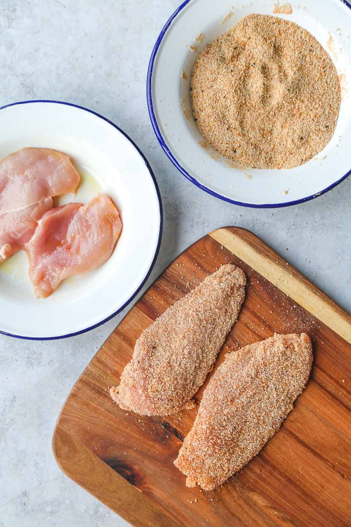 breaded raw chicken cutlets on a wooden board