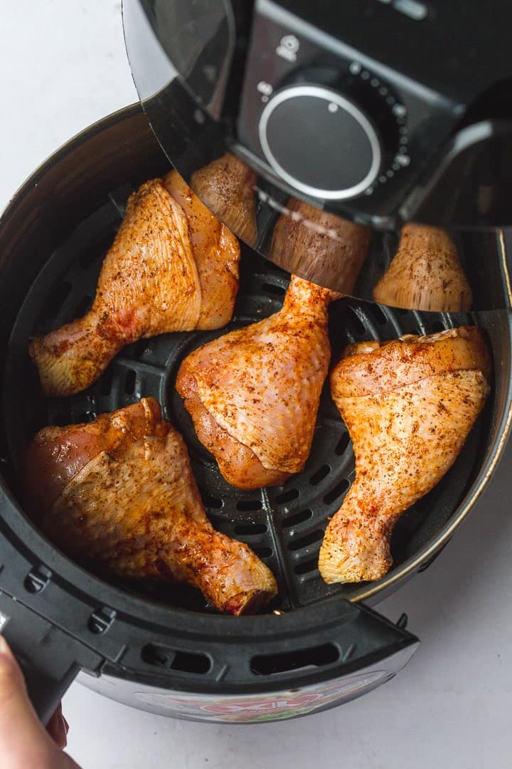 Placing the seasoned drumsticks in an air fryer basket.