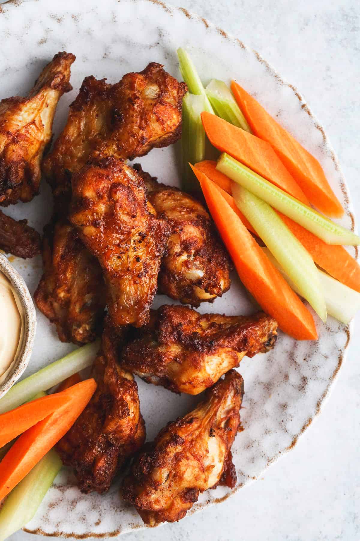 Crispy chicken wings in a plate, with carrot and celery sticks.