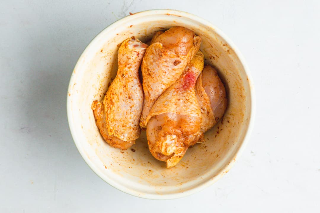 Raw and seasoned chicken legs in a bowl.
