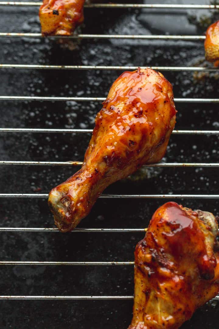 A chicken drumstick glazed with BBQ sauce on a baking sheet rack.