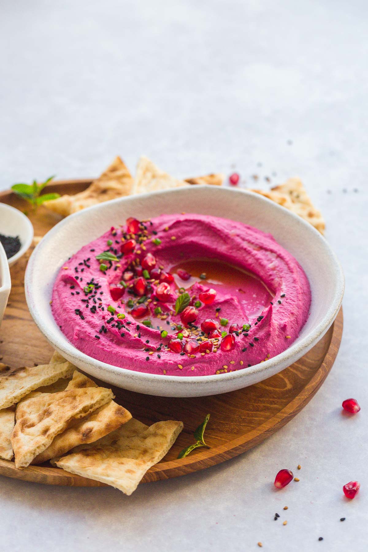 A bowl with Creamy Beet Hummus on a wooden tray with pita chips