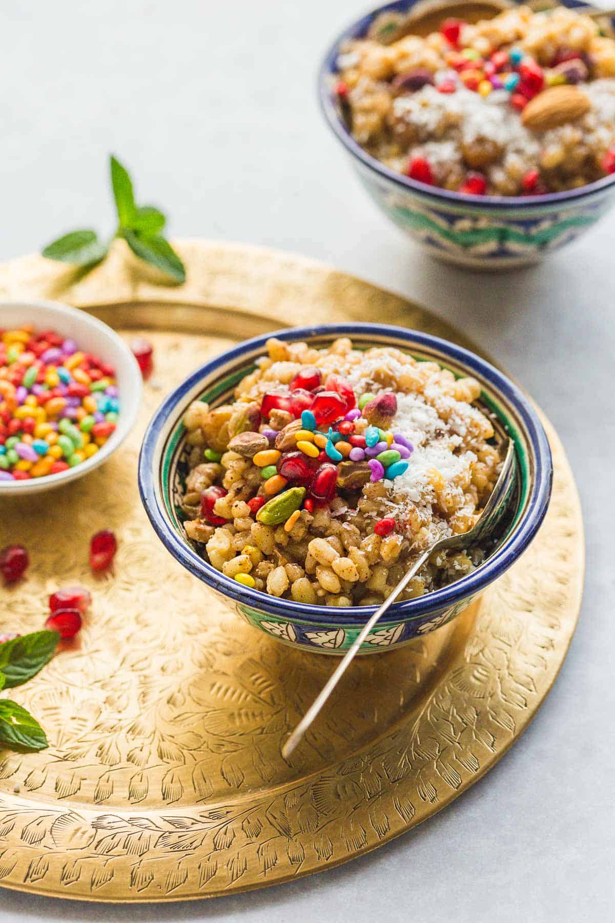 2 bowls of burbara wheat berry dessert with toppings on a golden tray