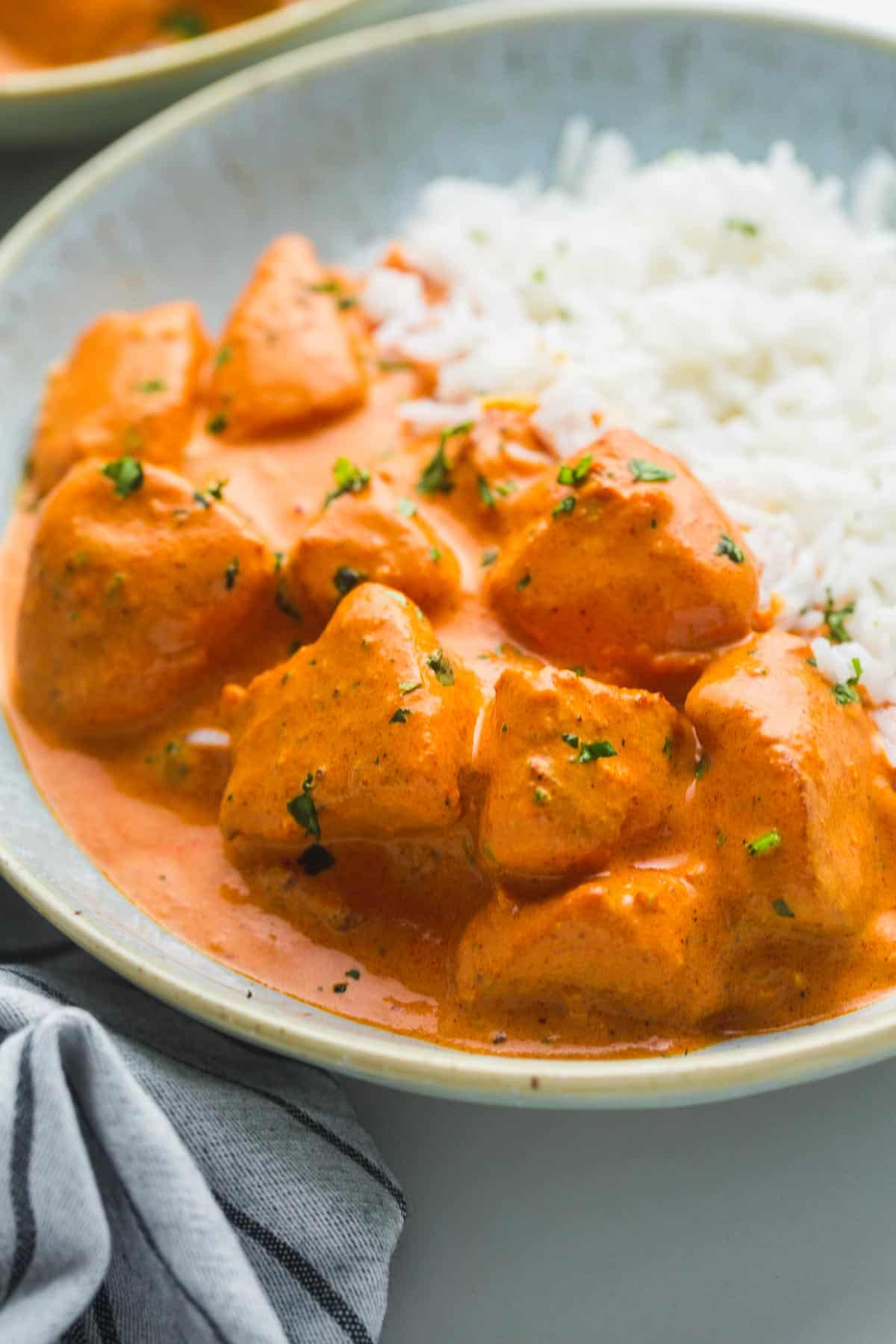A close up of butter chicken in a bowl served with basmati rice