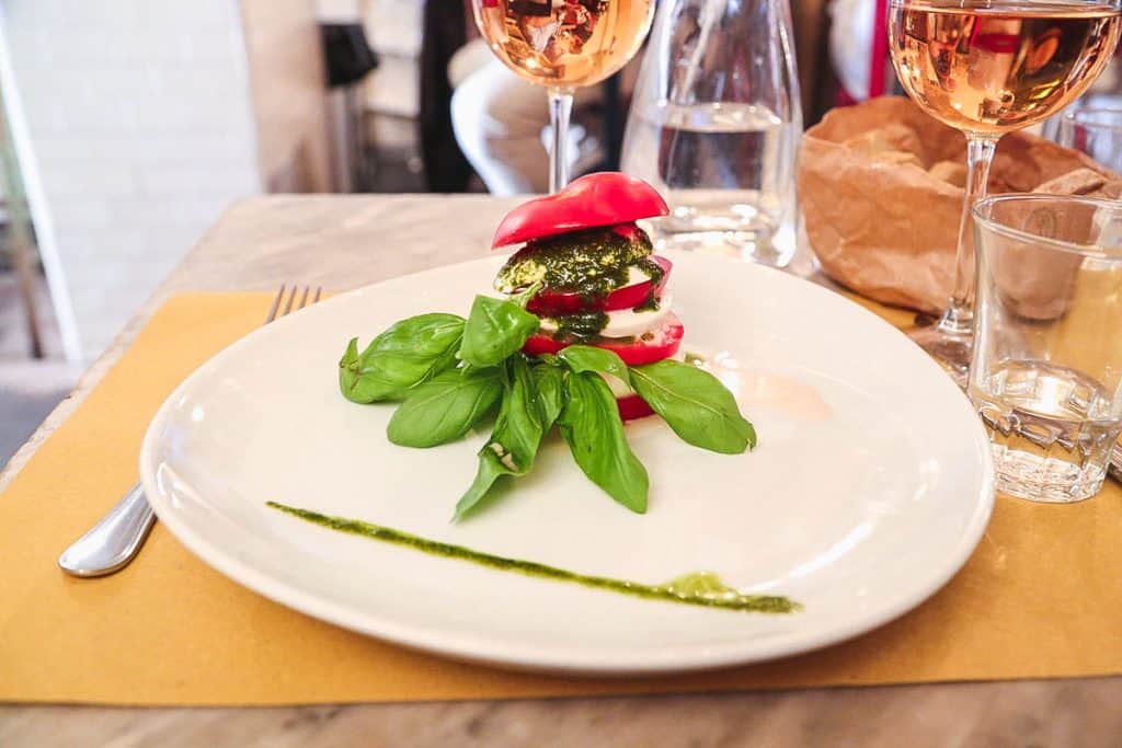 Caprese salad with tomato, fresh mozzarella, basil, and pesto served on a white plate in Rome