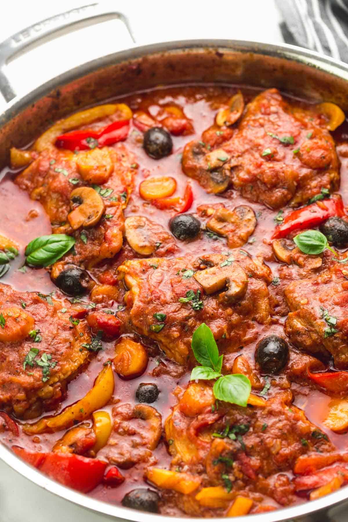 Chicken cacciatore in a skillet, garnished with fresh basil leaves