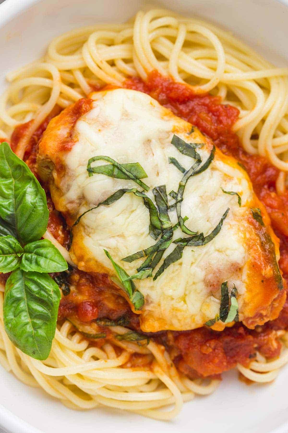 An overhead shot of chicken parm served over spaghetti, and garnished with chopped basil leaves