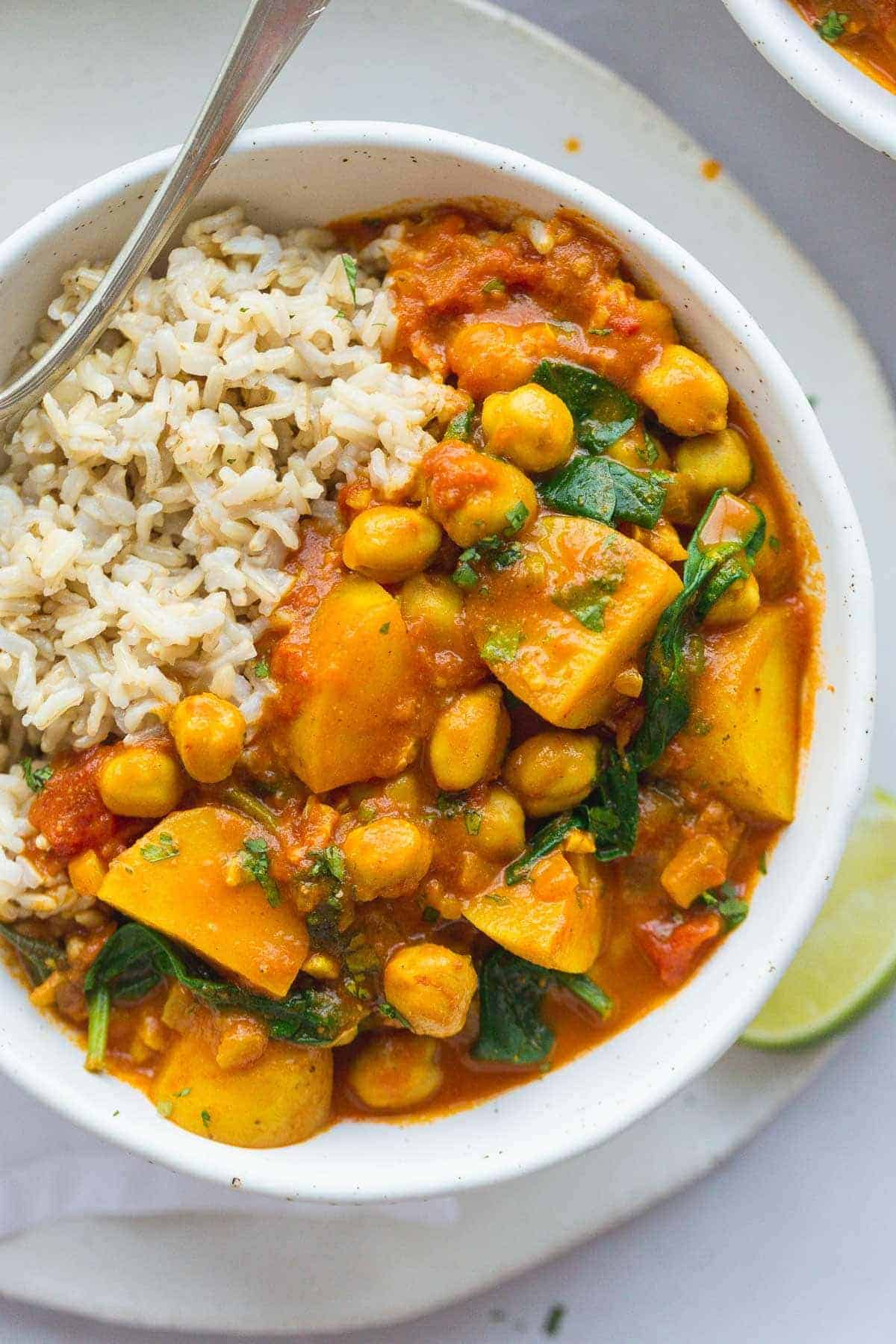 A close up shot of a white bowl with curry and brown rice