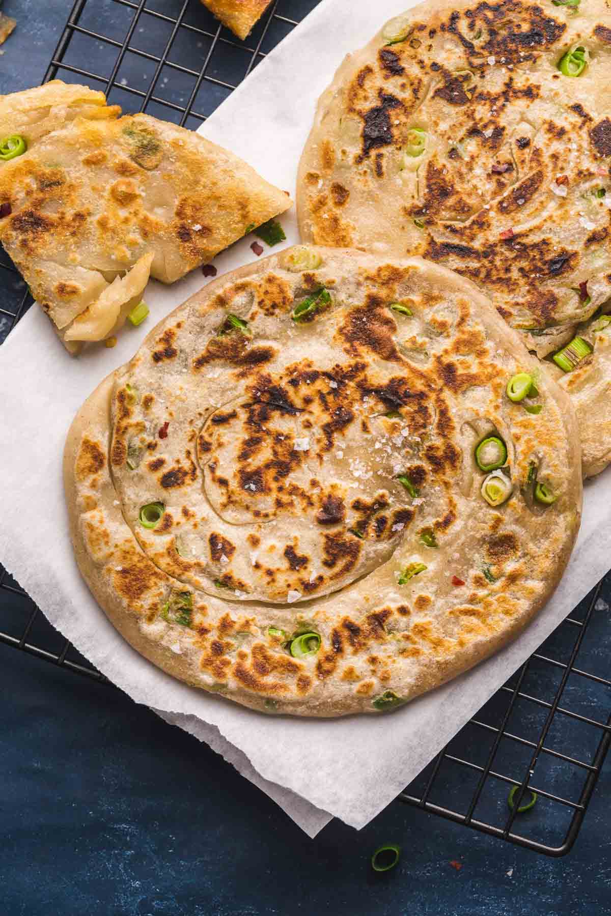 2 large scallion pancakes laid on parchment paper, and a quarter on the side