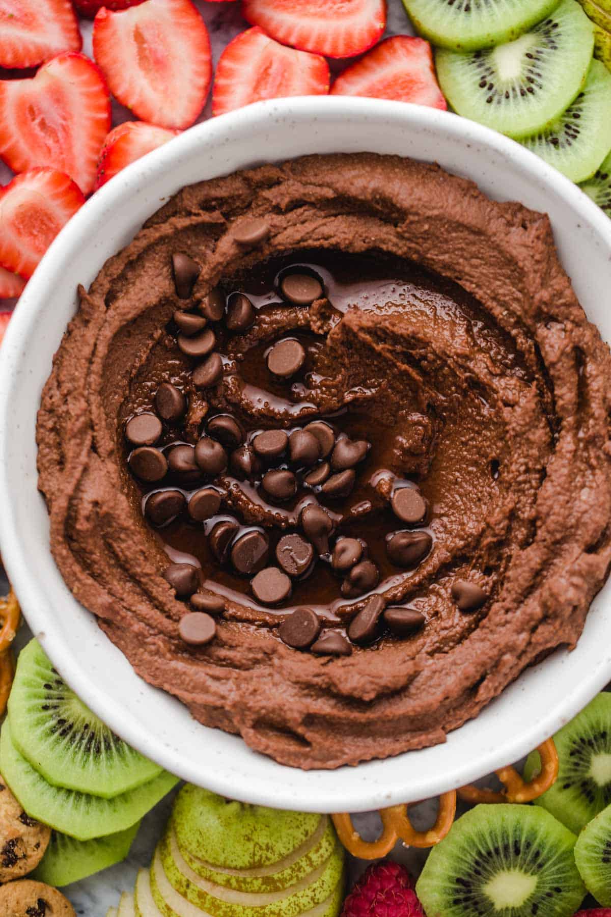 Chocolate hummus in a white bowl, with chopped up fruit on a platter