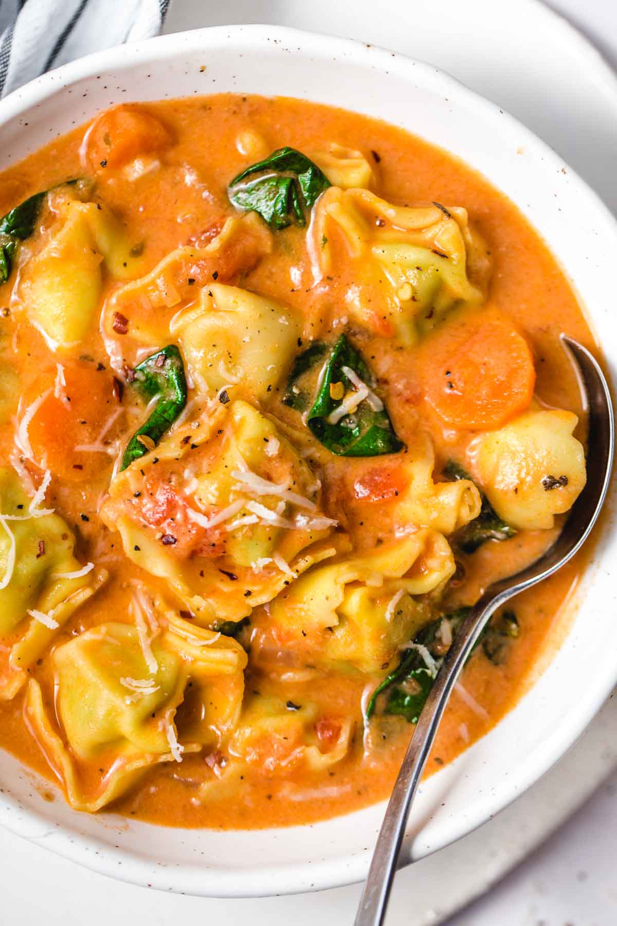 A bowl of creamy tortellini soup and a spoon