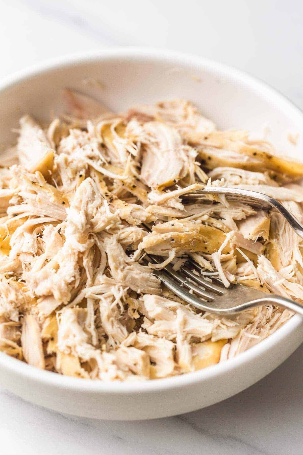 Crockpot Shredded Chicken in a white bowl with 2 forks