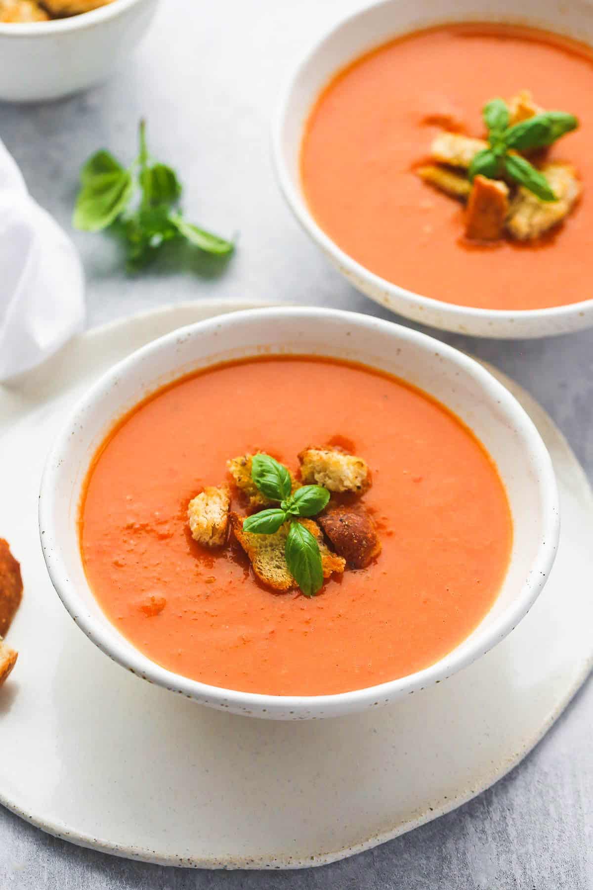 tomato soup in a 2 white bowls, with garlic croutons and fresh basil leaves