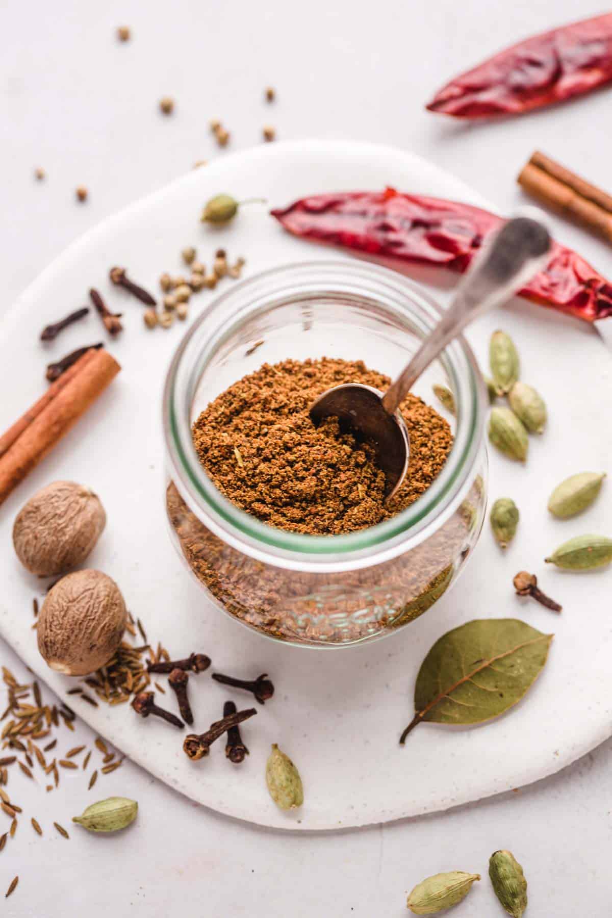 A small Weck jar filled with Garam Masala and a small teaspoon