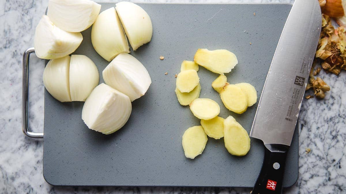 Grey cutting board, with sliced ginger, onion and a Zwilling chef knife