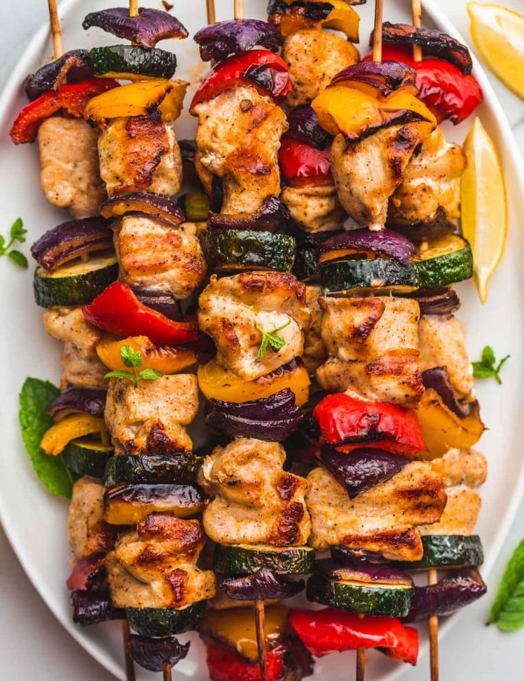 Grilled chicken kabobs with vegetables on a white platter