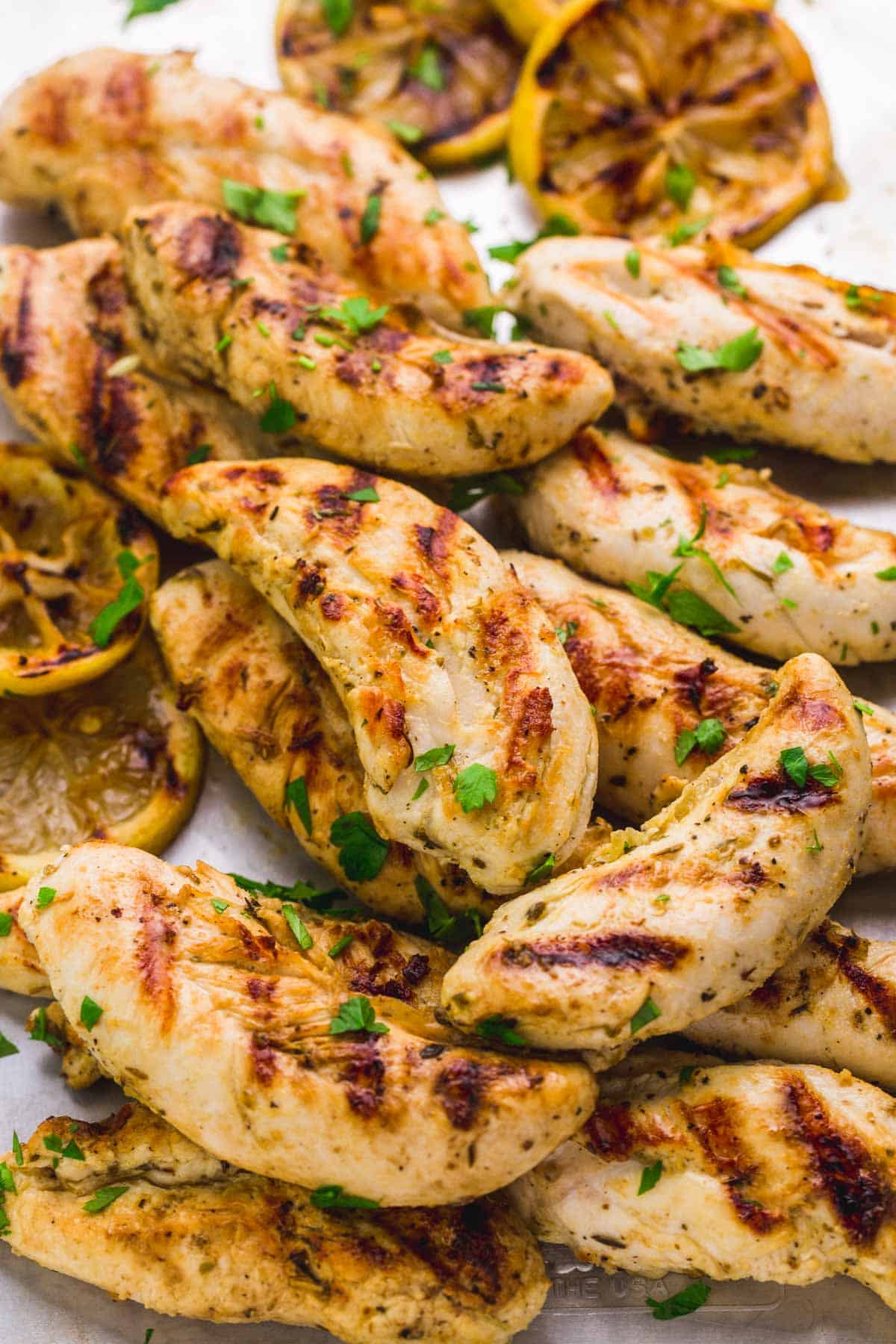 Grilled chicken tenders on a tray with chopped parsley