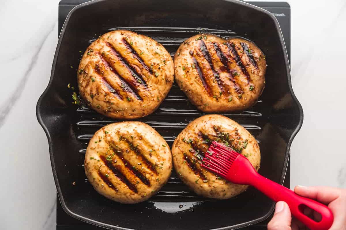 Basting the portobello mushrooms with more marinade as they're being grilled in a grill pan