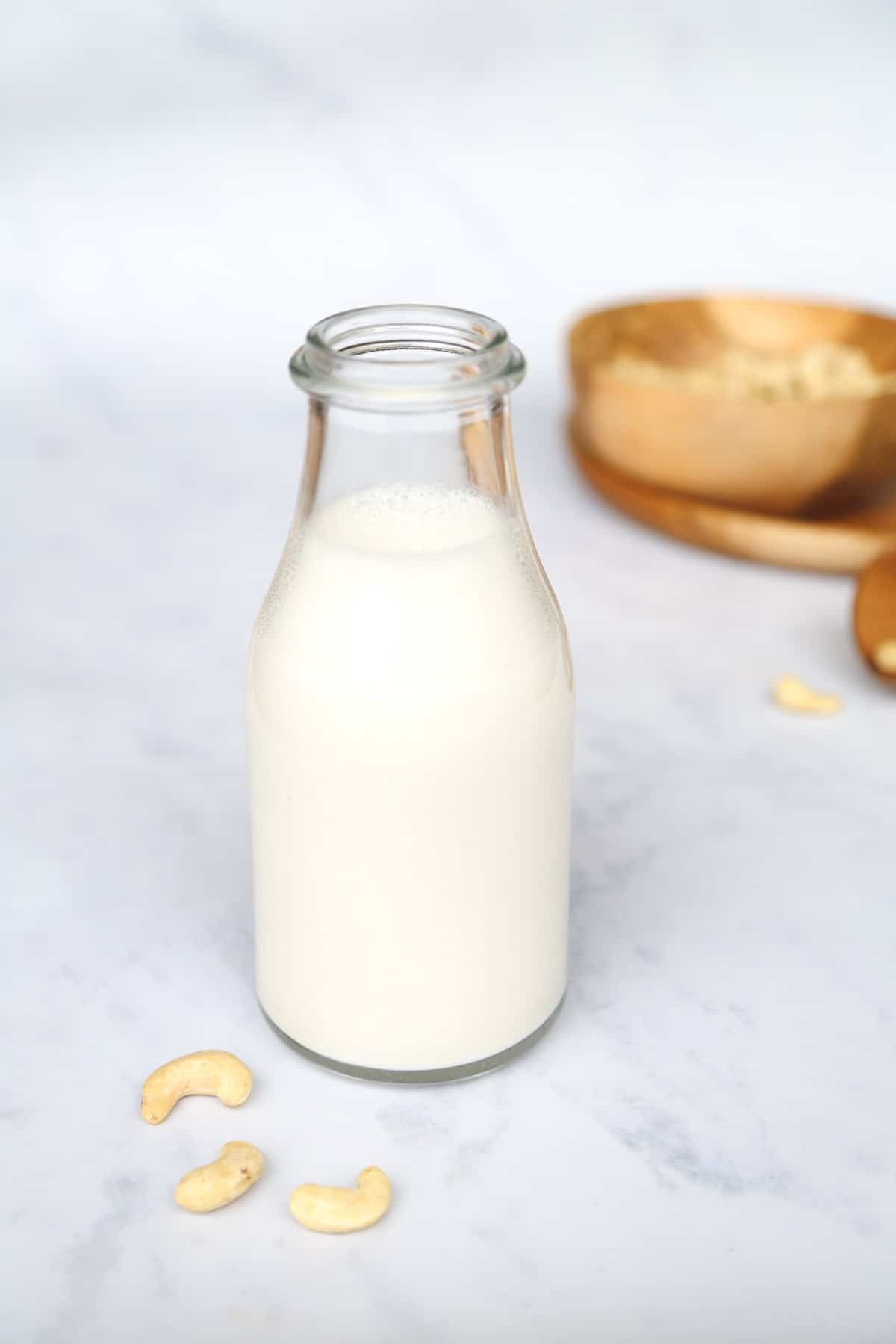 Creamy homemade cashew milk in a glass bottle, with some cashew nuts on the counter