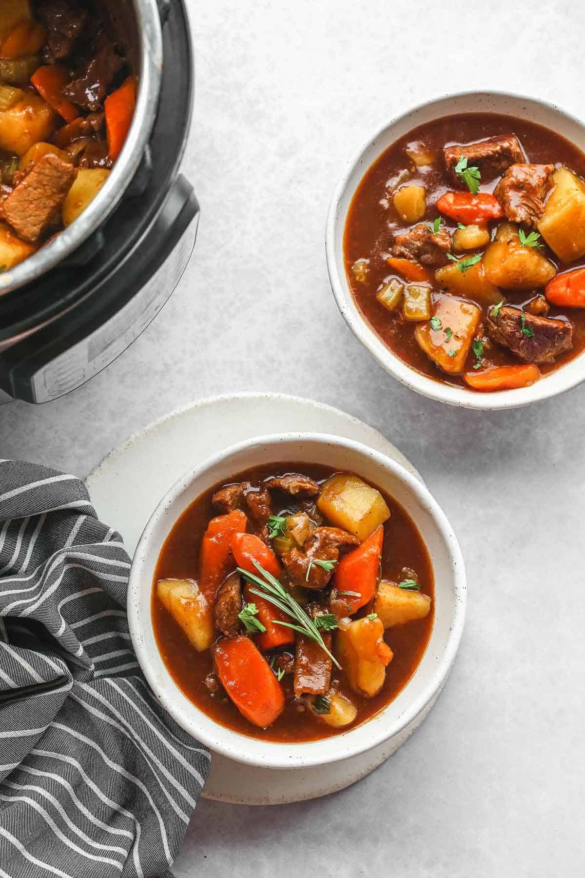 Instant beef stew in white bowls, and an Instant Pot with more beef stew