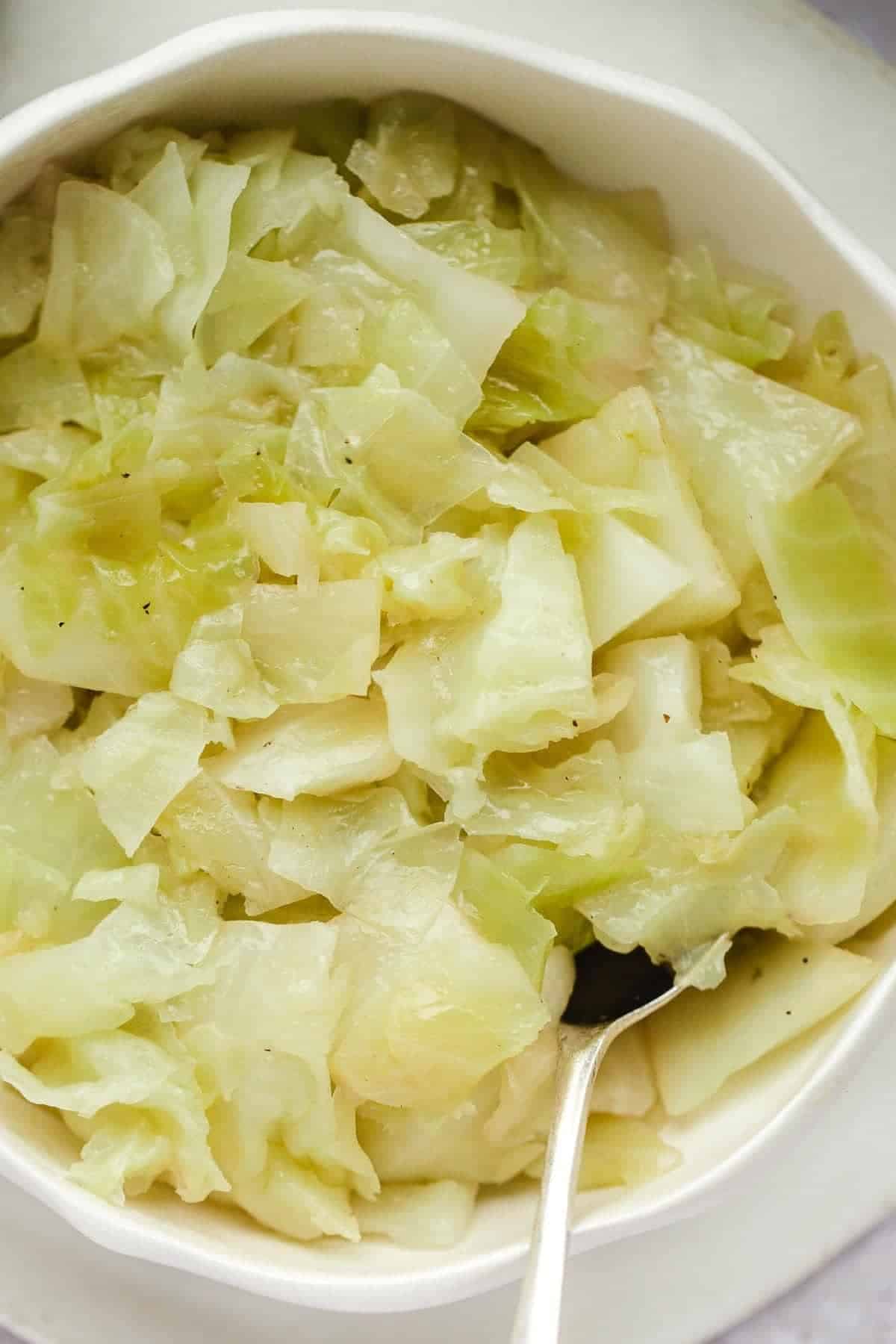 A close up of buttered cabbage in a white bowl with a metalic serving spoon