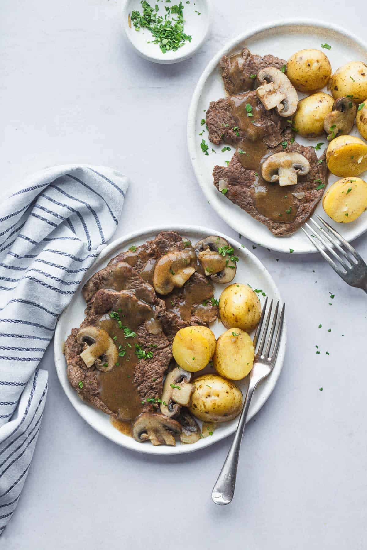 2 white plates with served Instant Pot cube steak, baby potatoes, and mushrooms