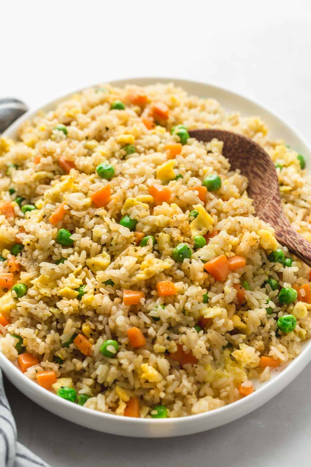 A large plate with fried rice served in it, and a wooden serving spoon