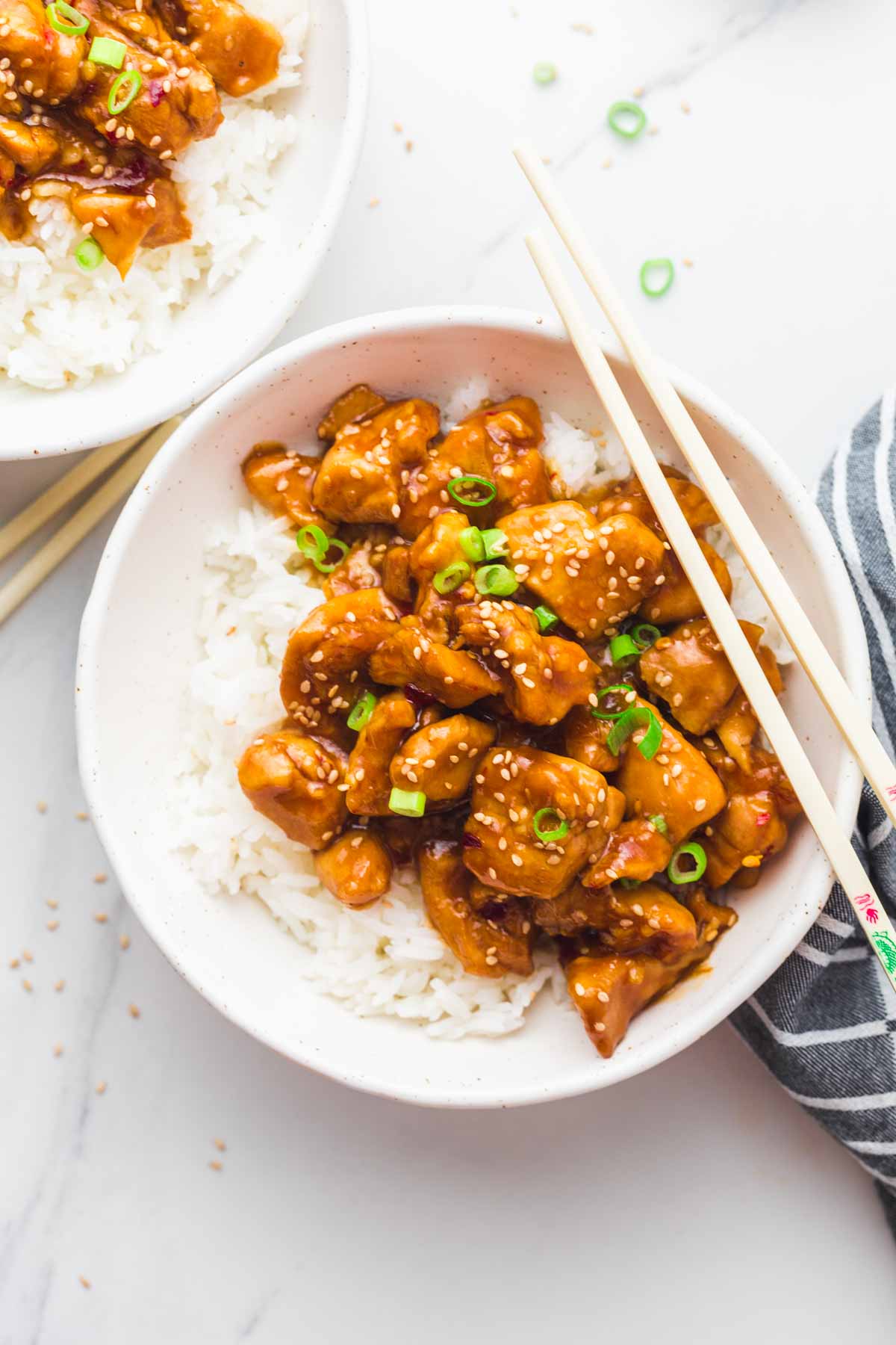 Glazed chicken served over steamed rice in white bowls, and chop sticks on the side