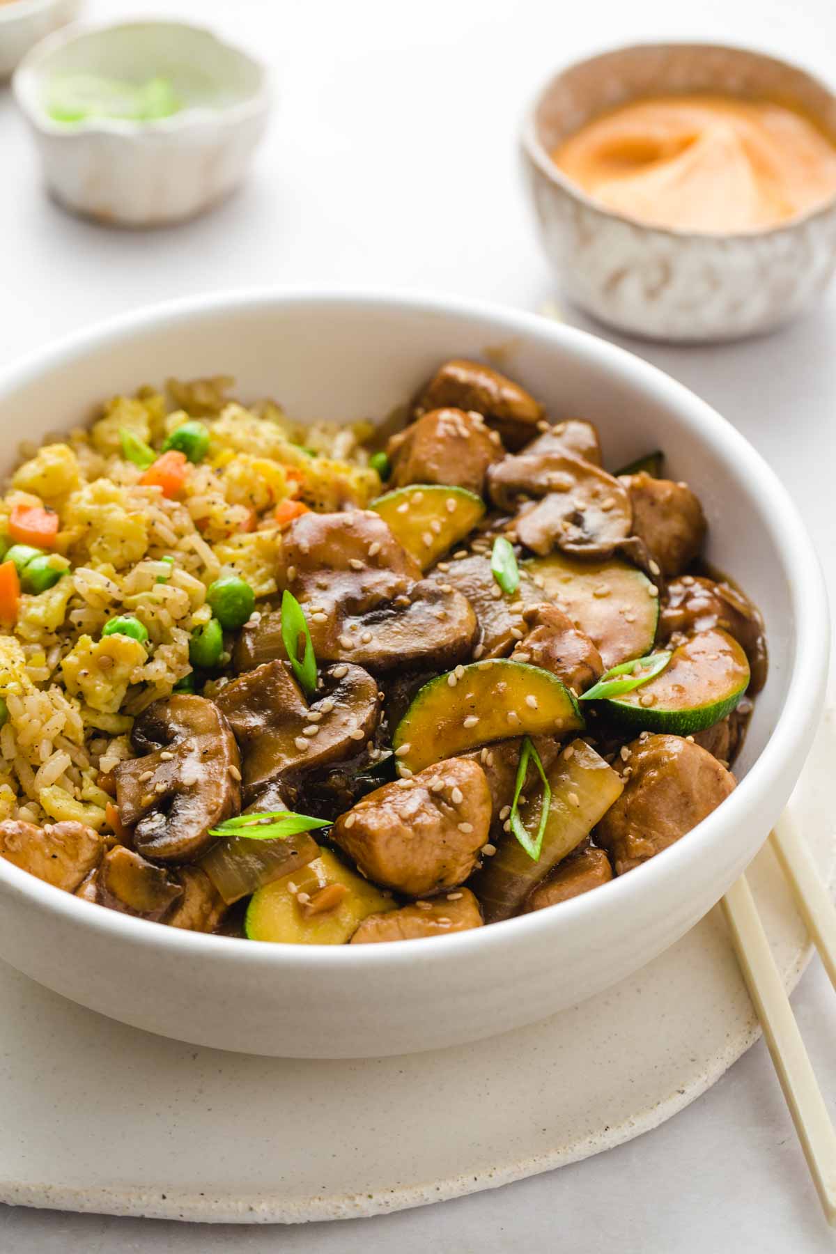 close up of hibachi chicken and hibachi rice in a white bowl, with sauces in the background