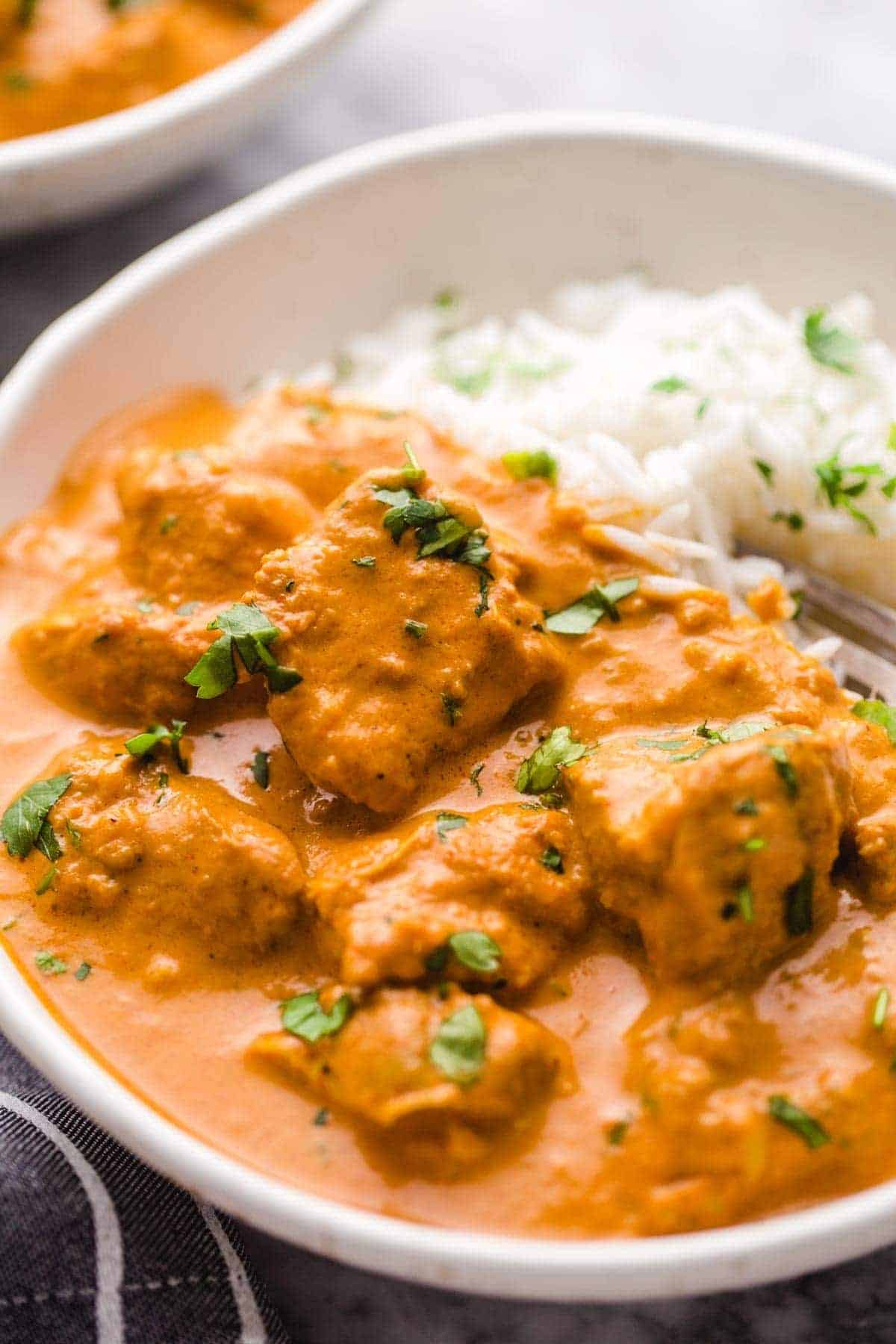 Butter chicken served with rice in a white bowl.