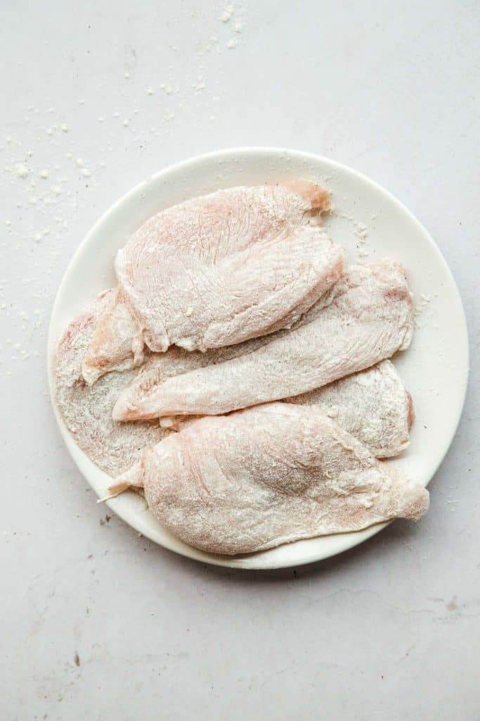 Raw chicken breasts covered in flour on a white plate