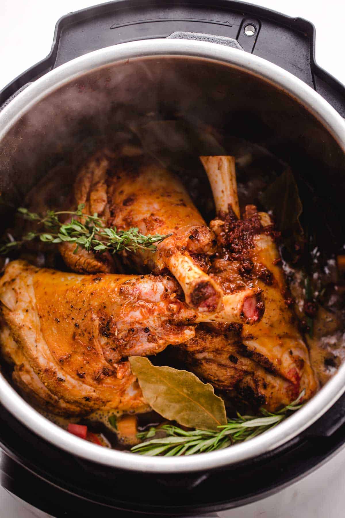 browned lamb shanks in the instant pot with fresh herbs and bay leaves