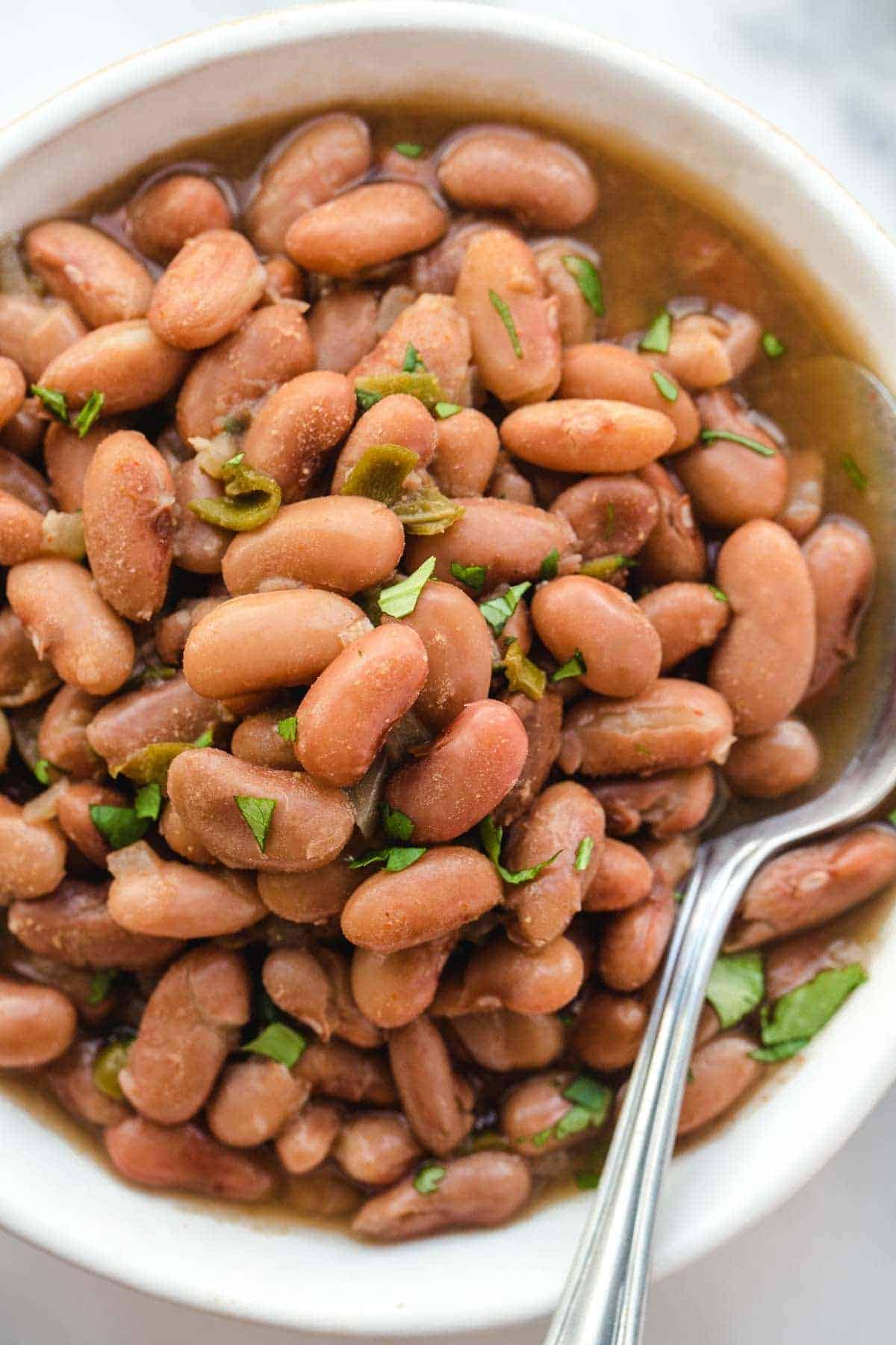 A close up of cooked pinto beans in a bowl with a spoon, garnished with fresh chopped parsley