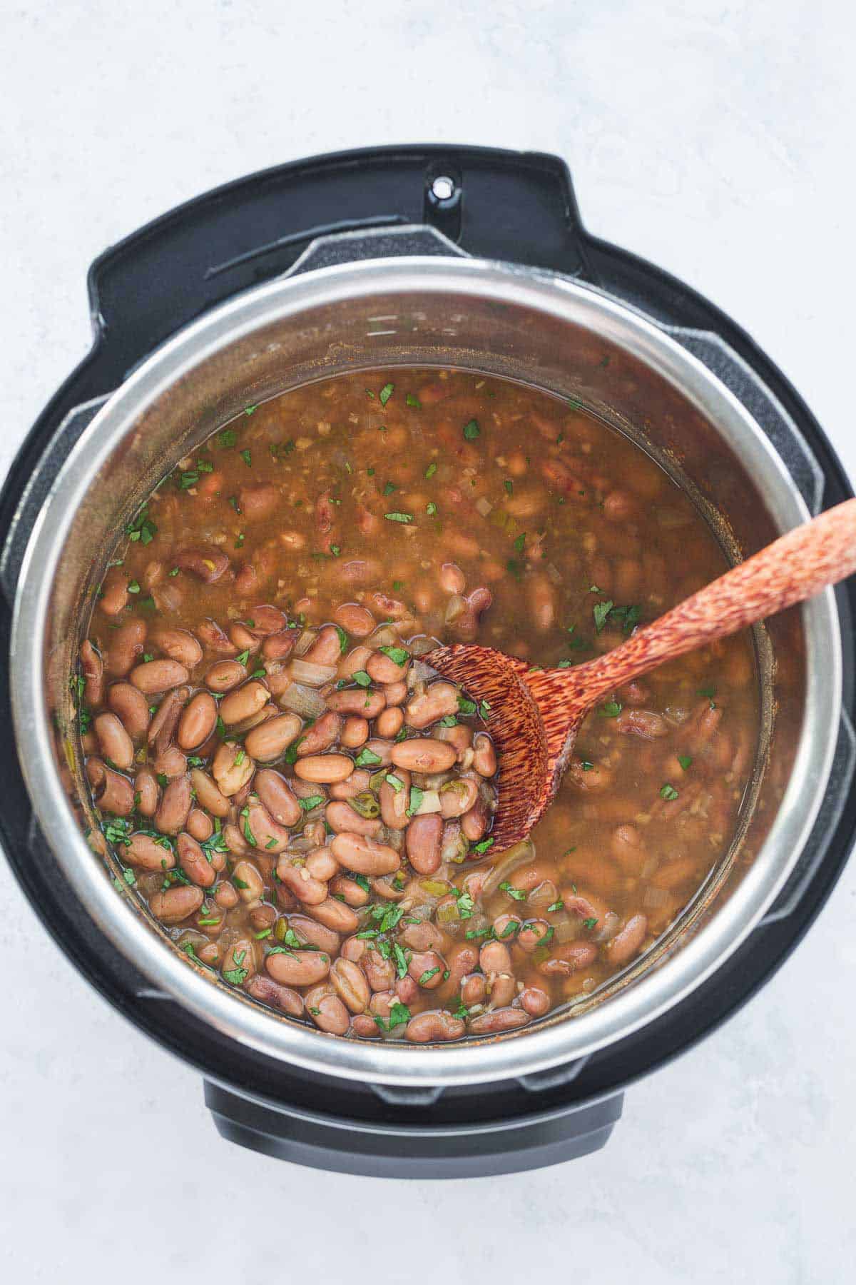 Cooked pinto beans in the instant pot with a wooden spoon