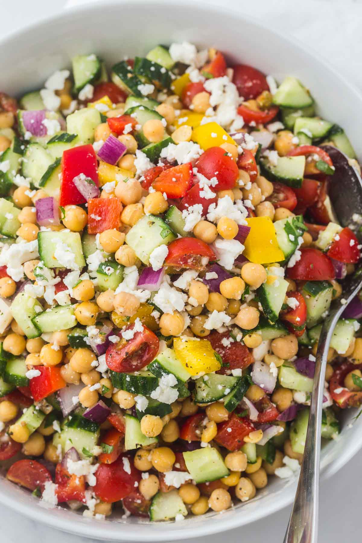 Mediterranean Chickpea Salad in a white salad bowl, and a serving spoon on the right side.