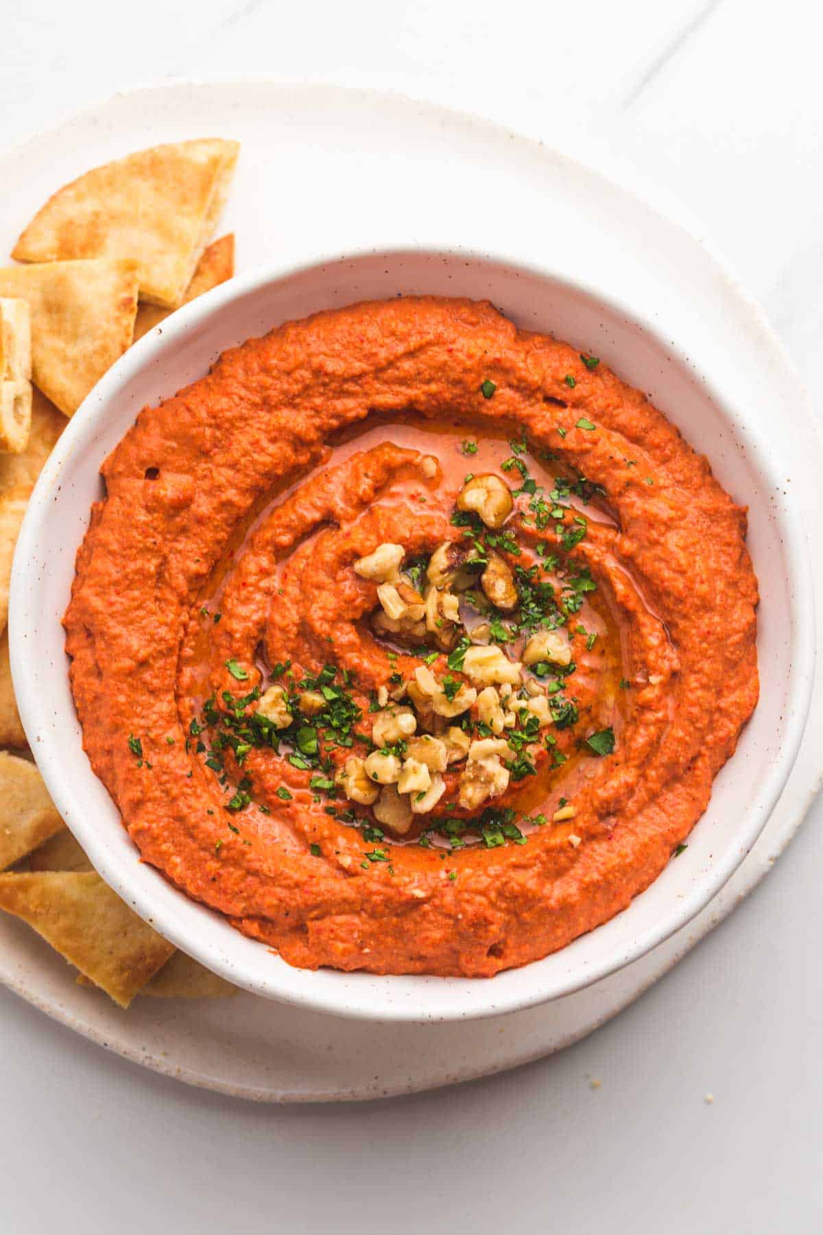 A white bowl with muhammara, and pita chips of the side