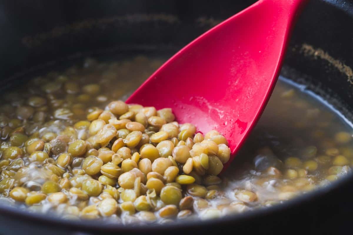 Cooked green lentils in a pot with a red spatula