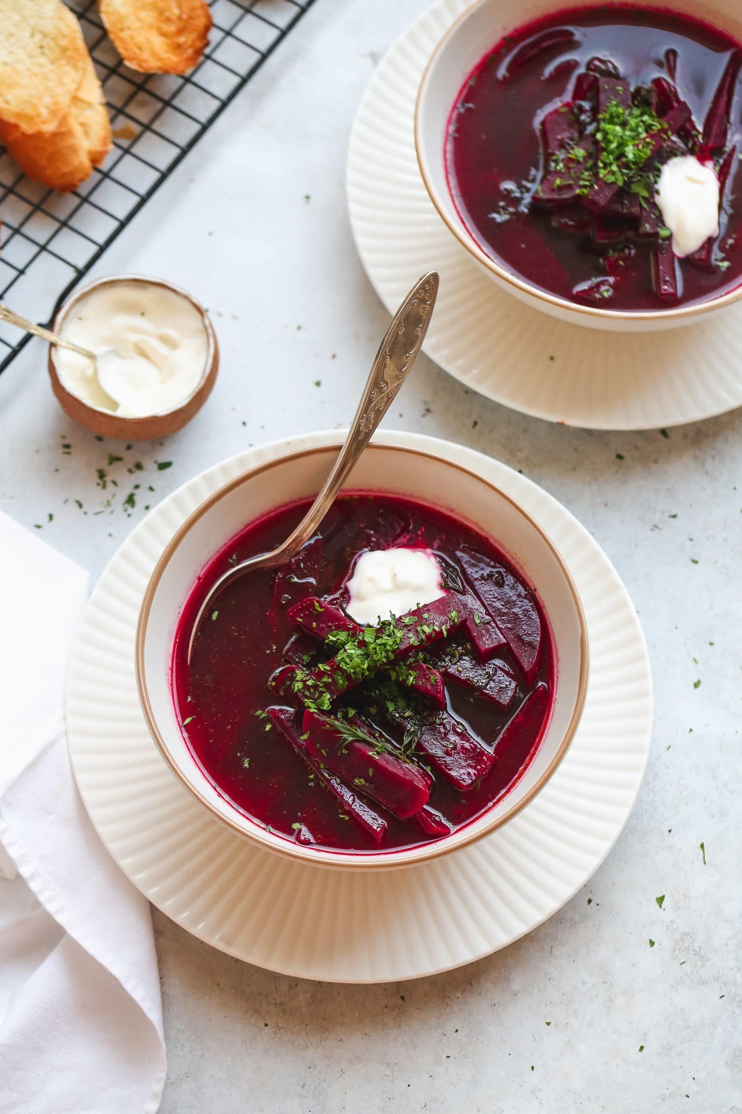 2 bowls of borsch beet soup with spoons, dollops of smetana and fresh parsley.