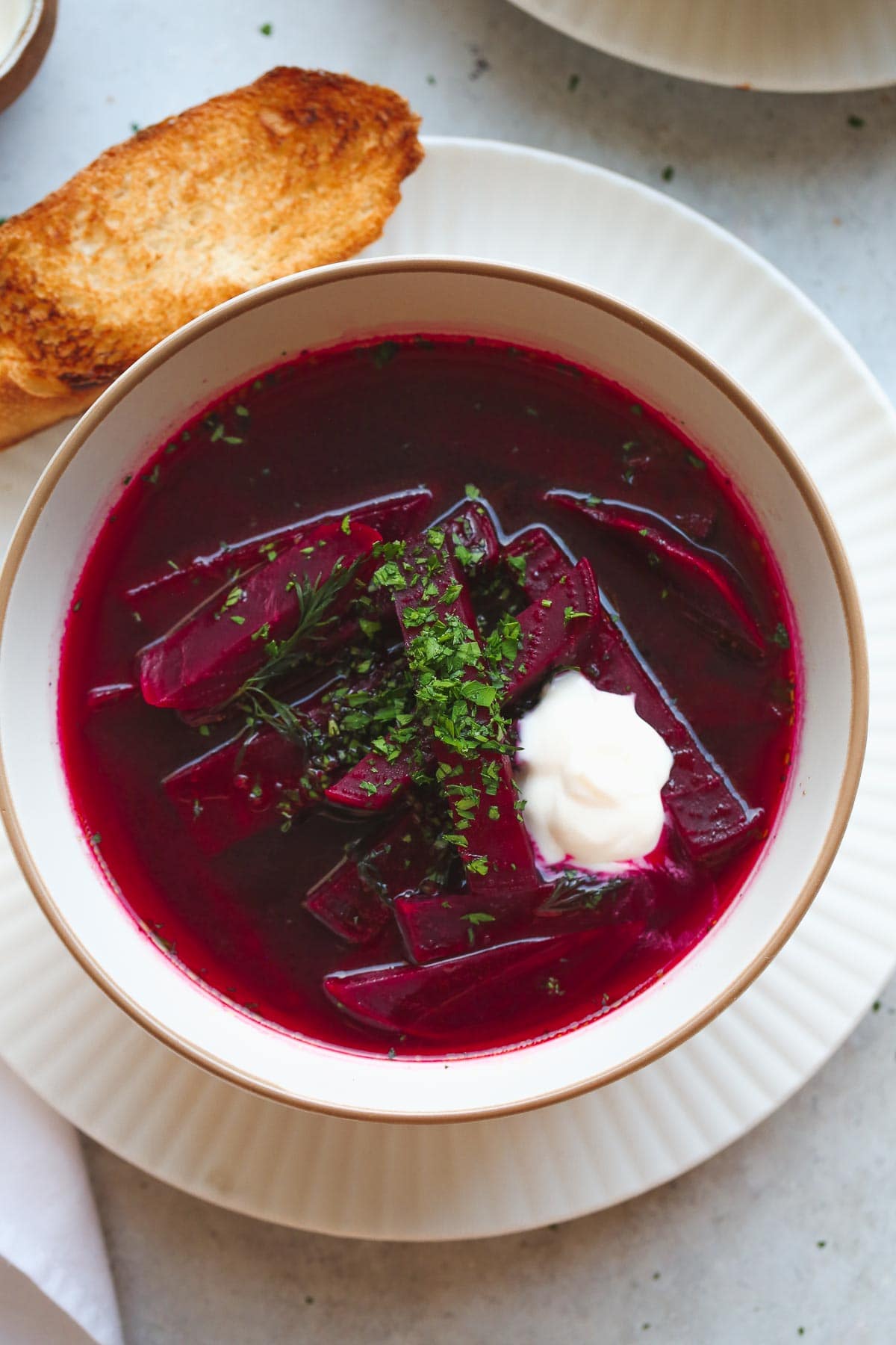 A close up shot of borsch beet soup with a dollop of smetana cream, garnished with chopped parsley