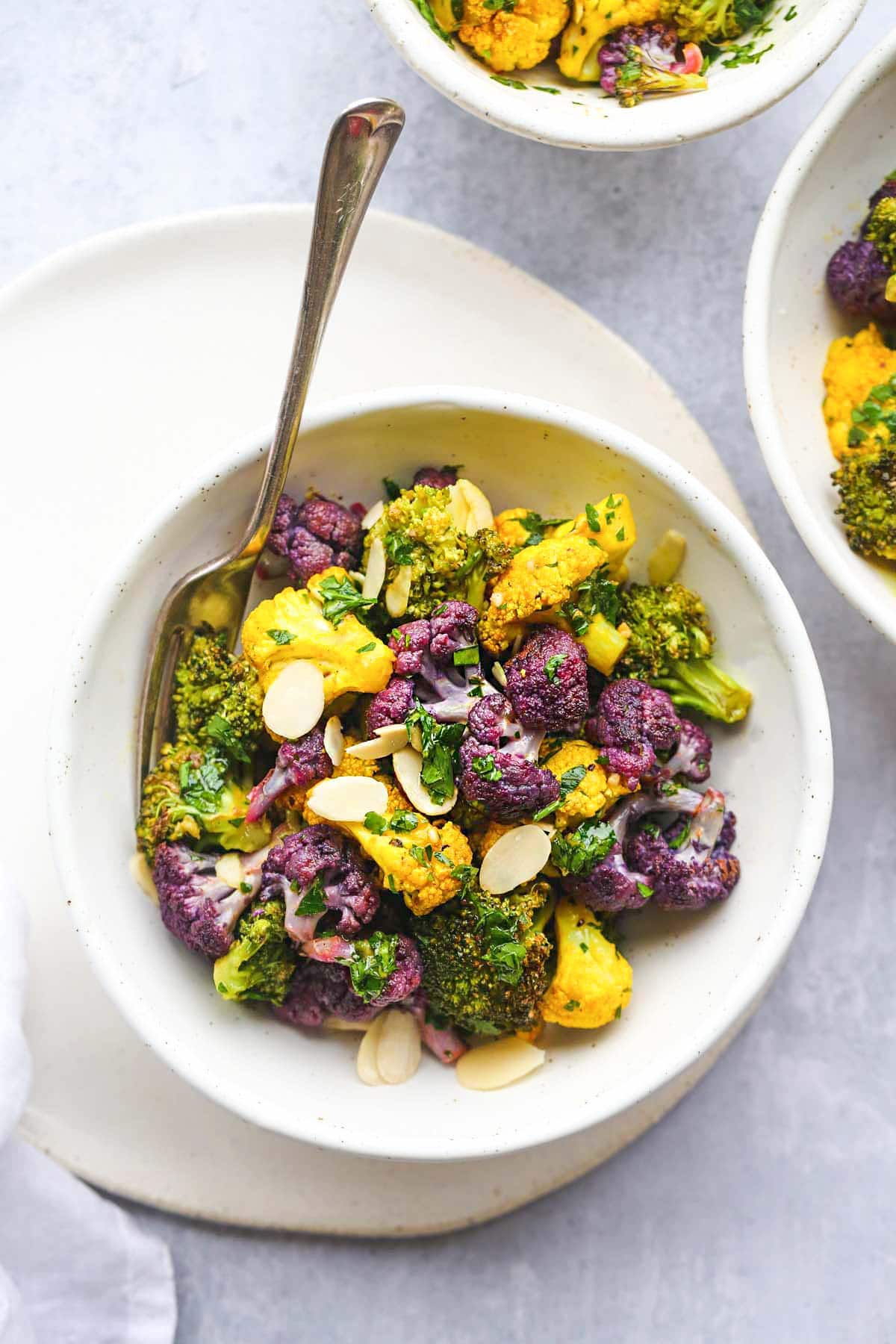 A white bowl of roasted purple cauliflower salad and a fork on the side