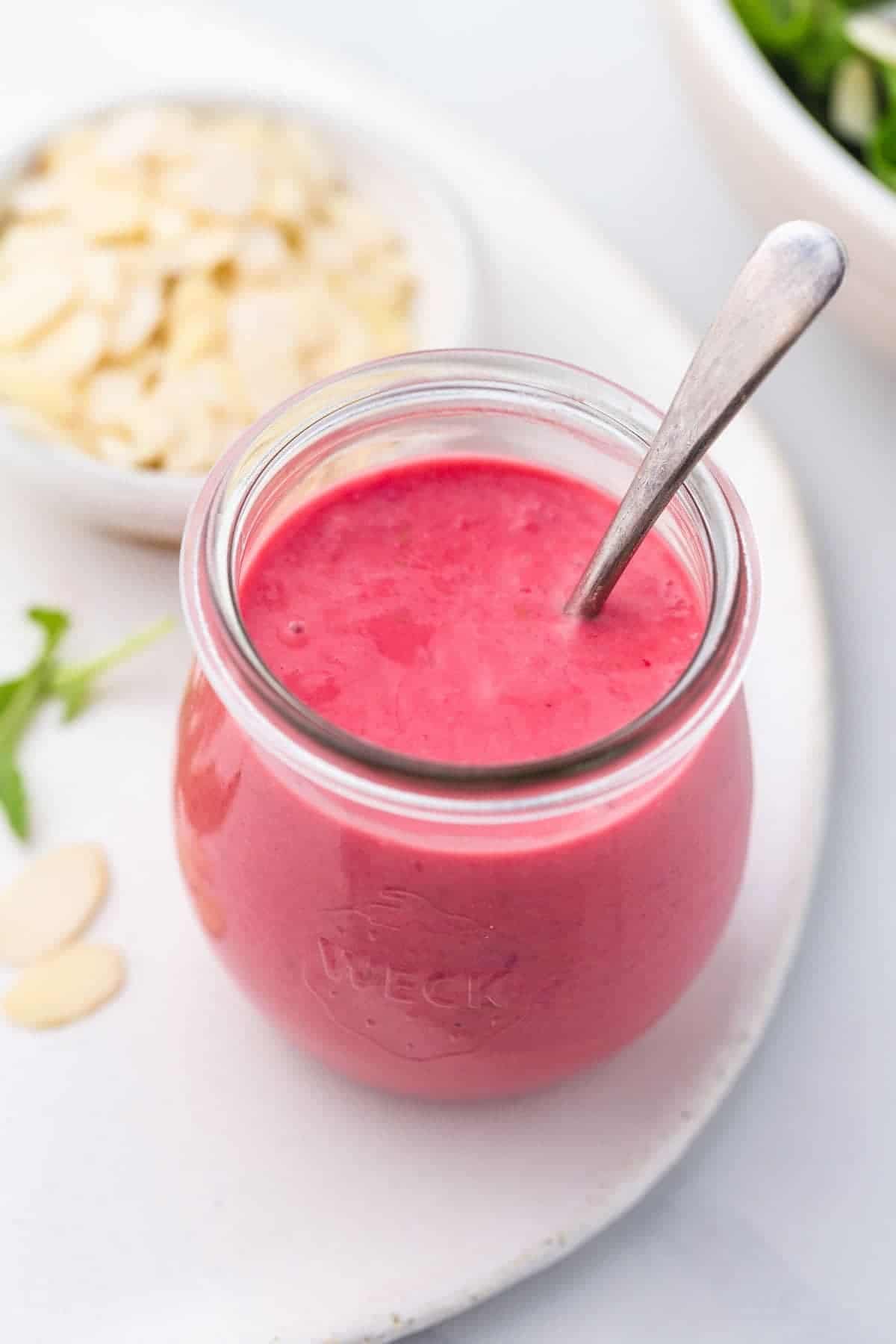 A small Weck jar with blended Raspberry Vinaigrette and a teaspoon