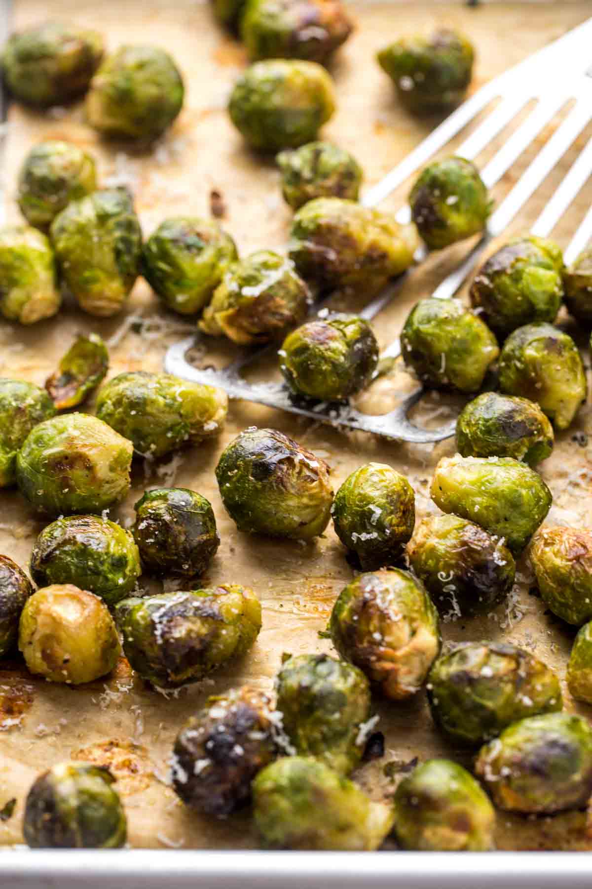 Roasted brussels sprouts on parchment paper, with a fish turner to flip them.