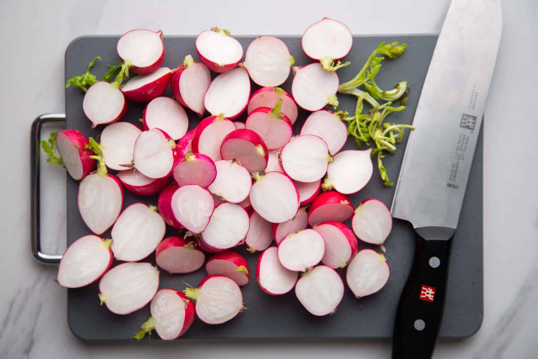 Sliced radish halves on a grey cutting board and a chef's Zwilling knife on the side