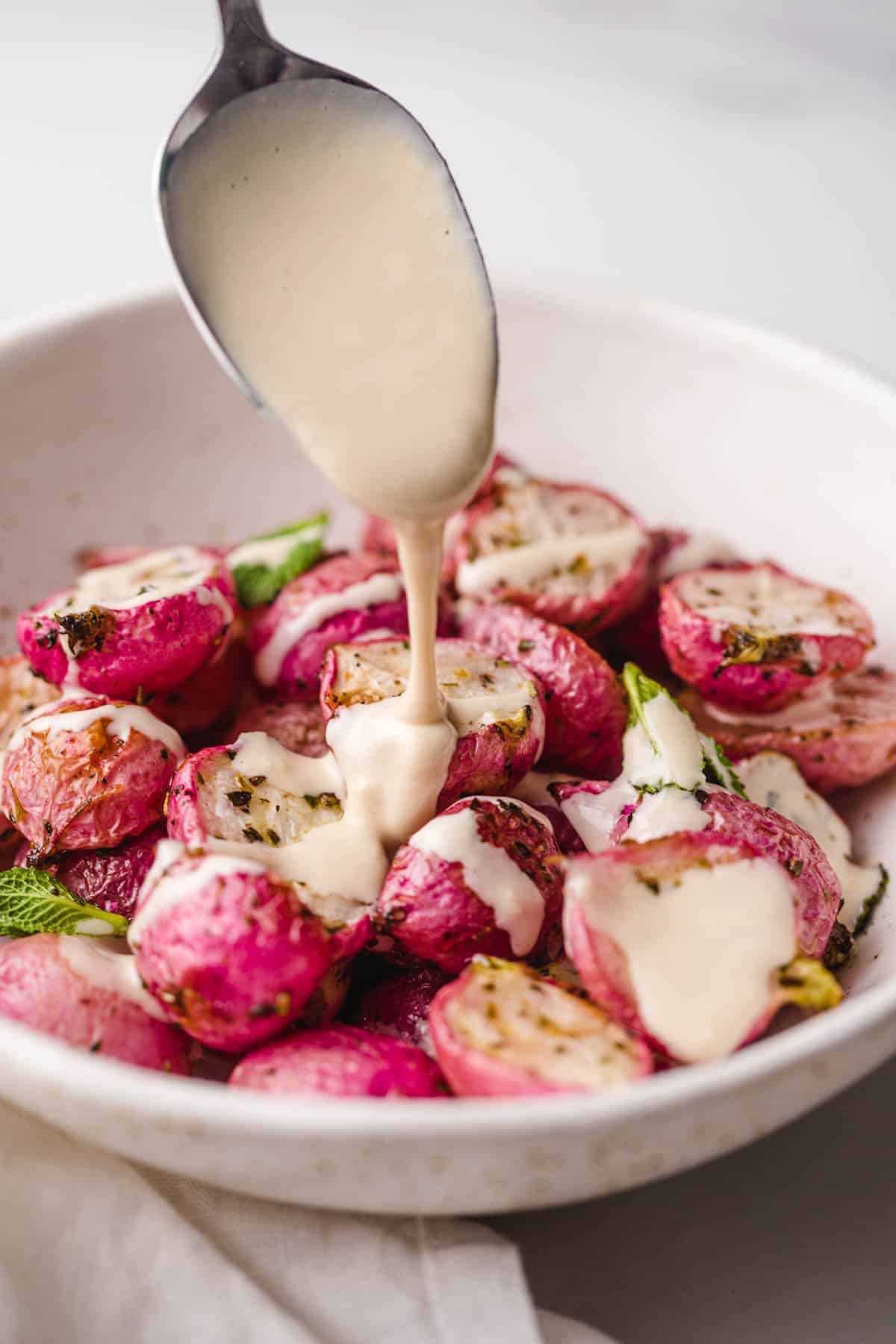 Drizzling creamy tahini sauce over roasted radishes