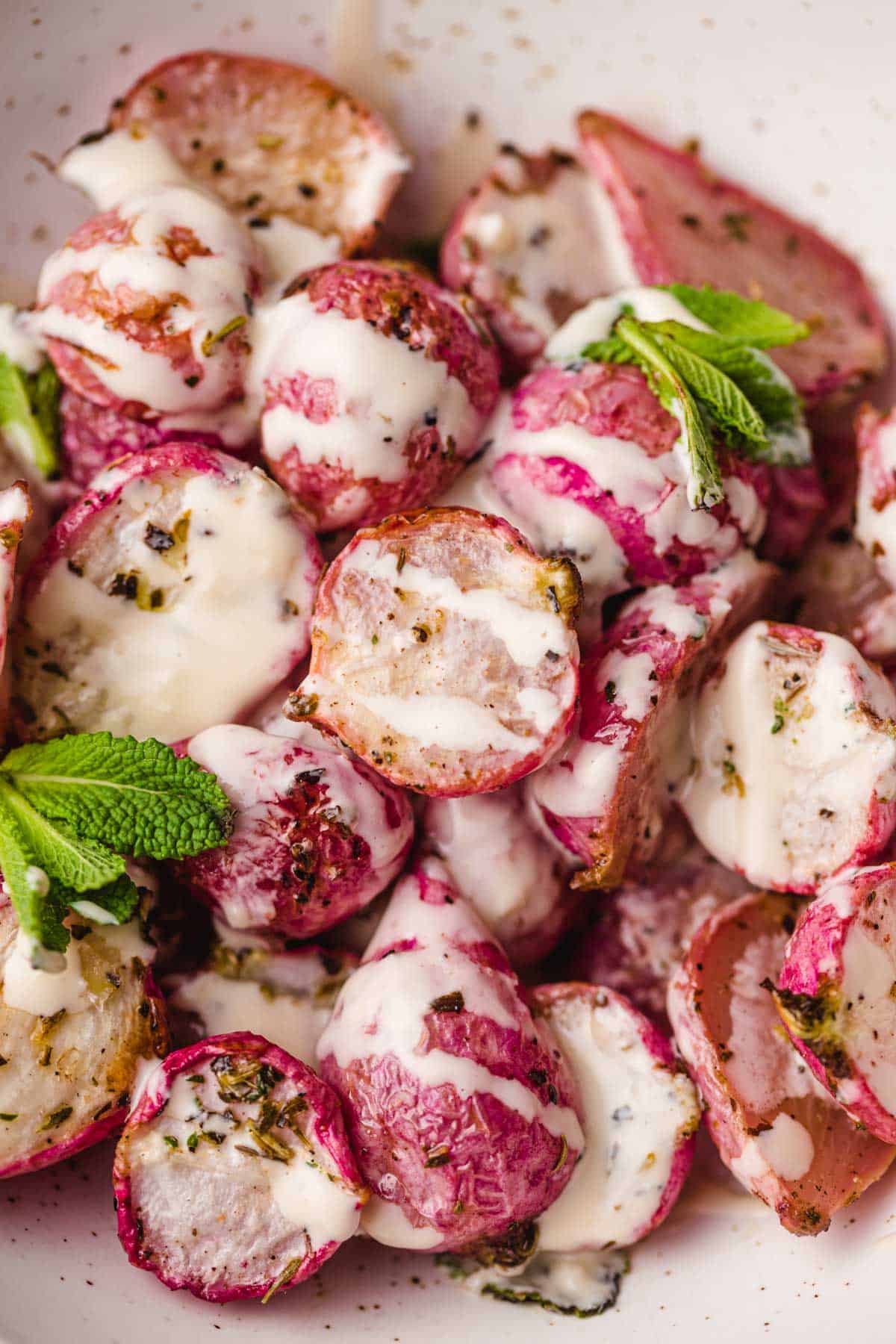A bowl of roasted radishes drizzled with creamy tahini garlic dressing