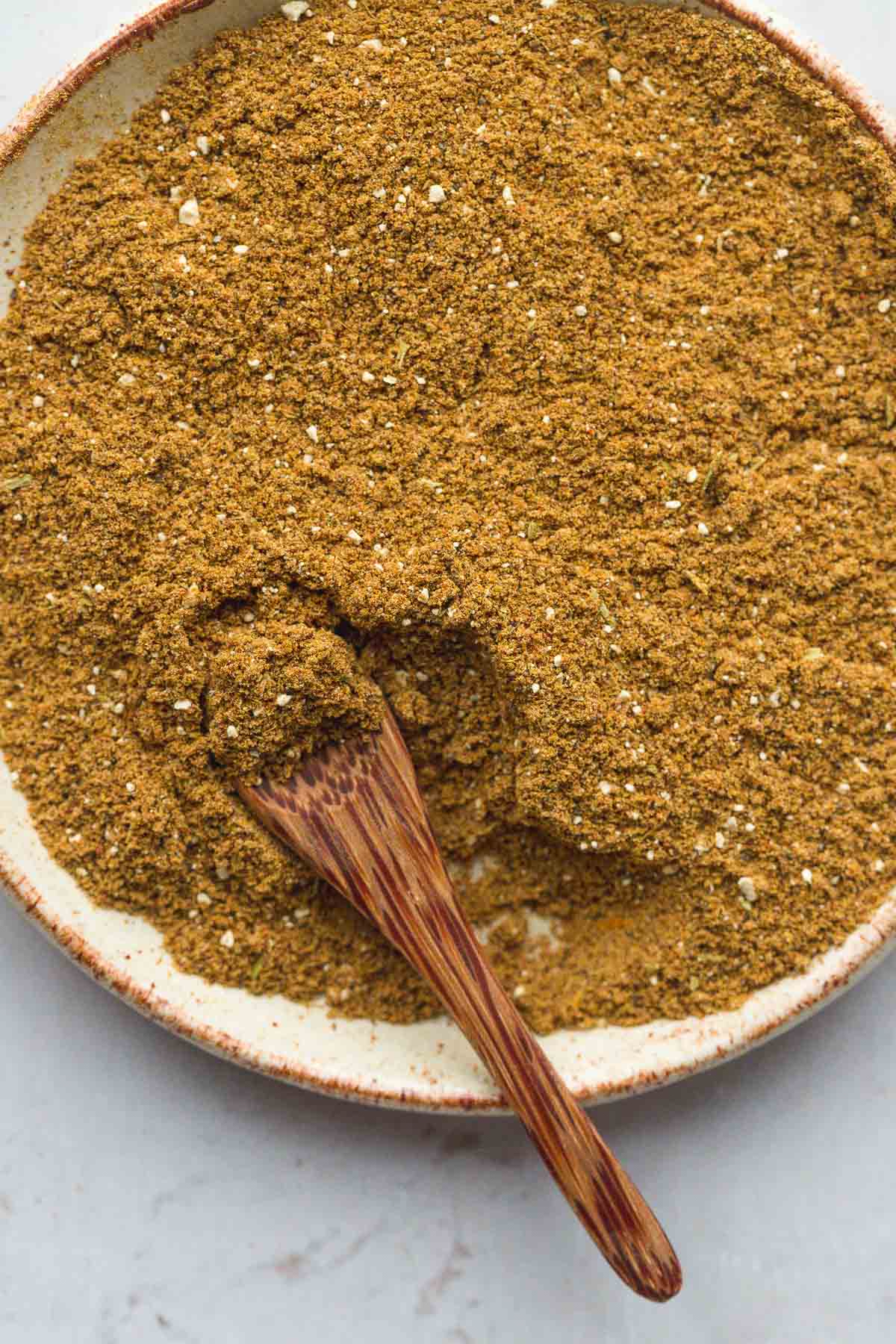 A close up of ground shawarma seasoning in a handmade small plate and a wooden spoon