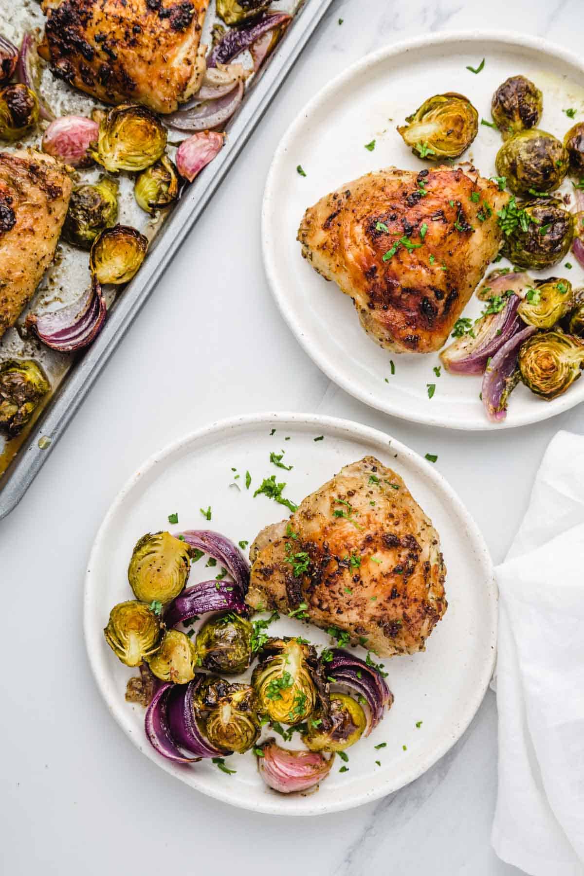 2 plates with sheet pan chicken thighs, brussels sprouts, roasted garlic and red onion.