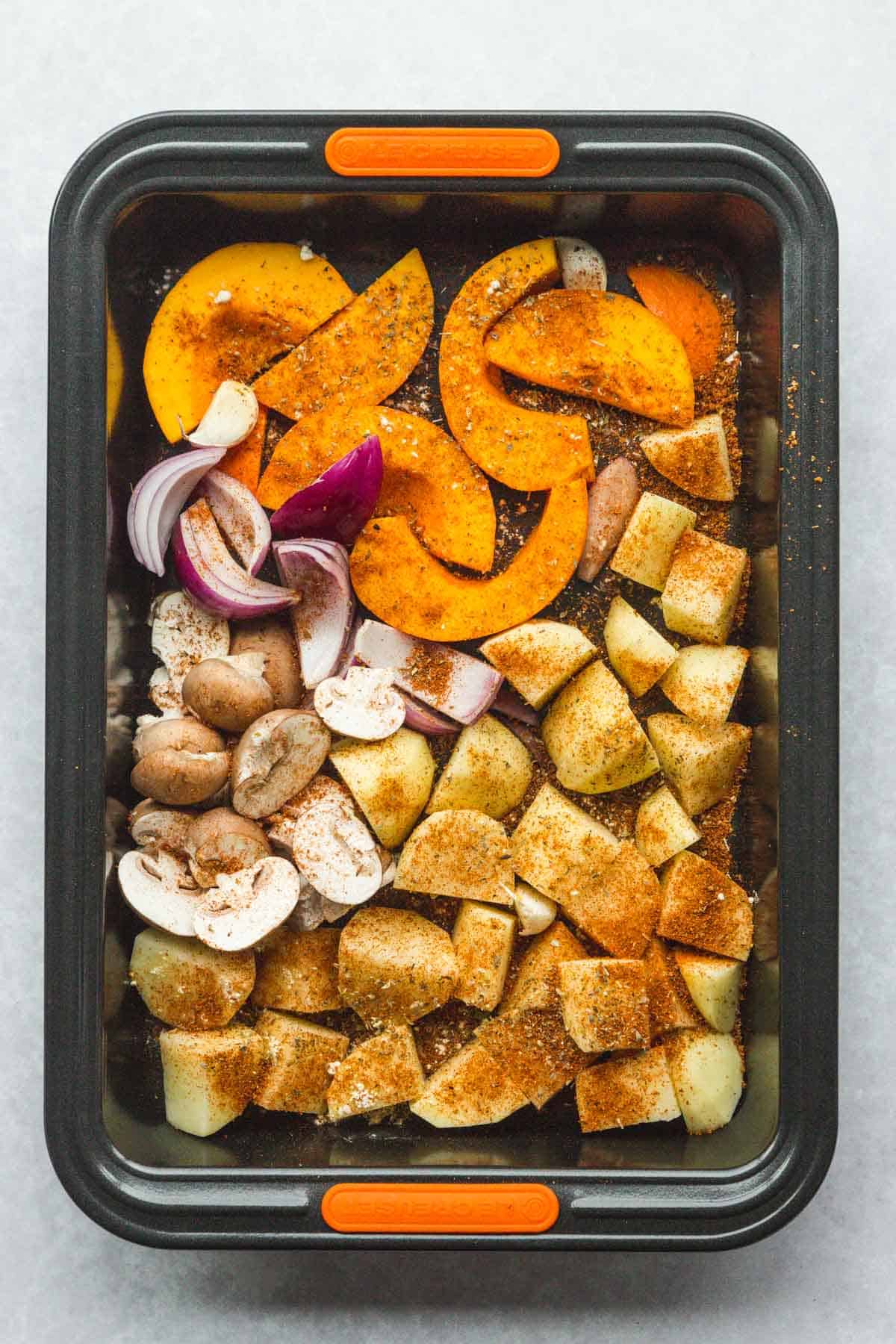 Chopped veggies in a roasting tin with seasonings and olive oil