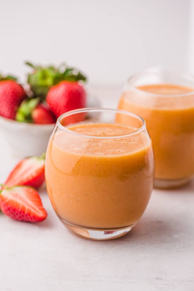 2 glasses of orange colored smoothie, and strawberries