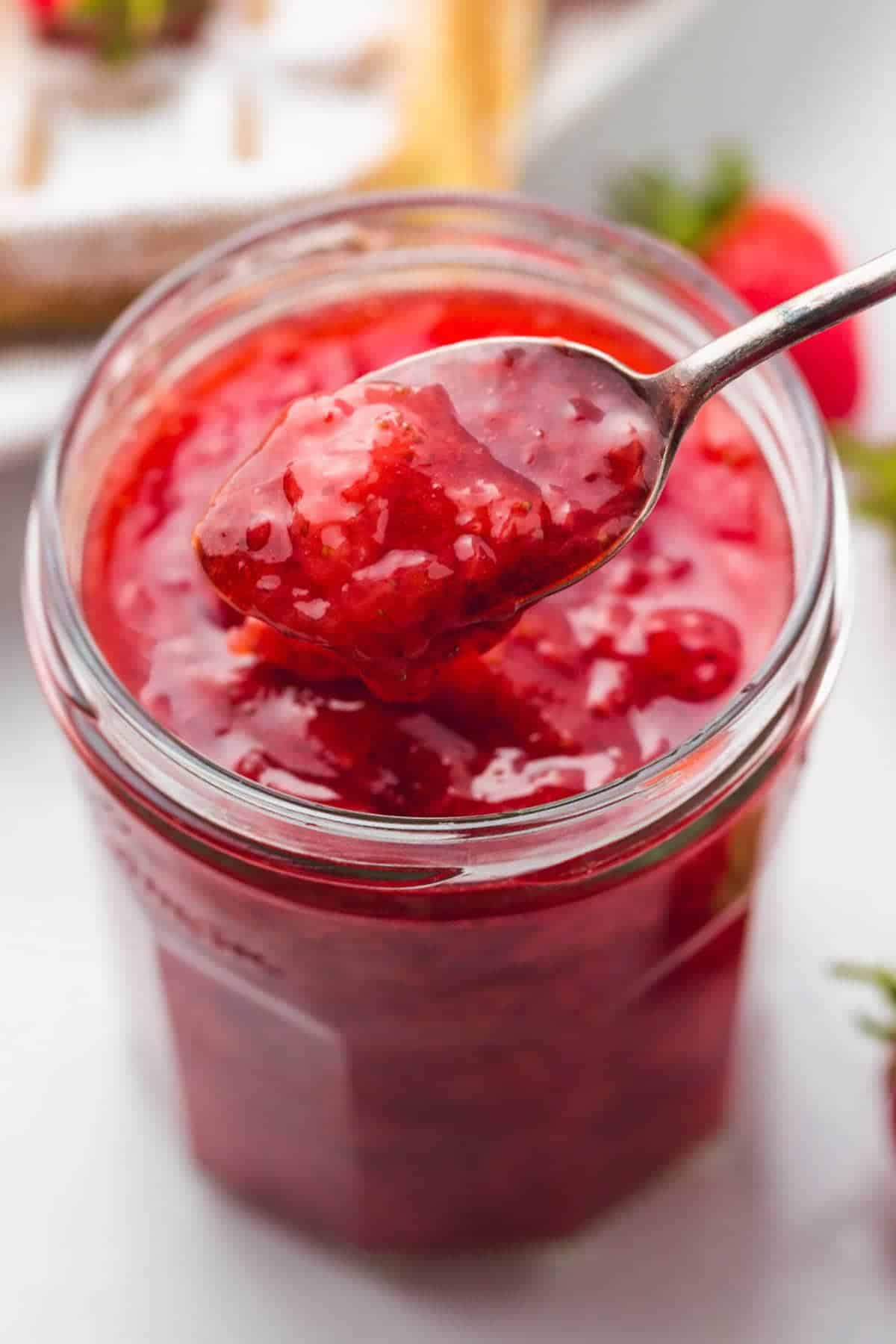 Close up of strawberry sauce on a spoon and a jar
